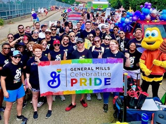 General Mills employees marching in Pride parade holding General Mills Celebrate Pride Banner alongside Cheerios Mascot, Buzz Bee.